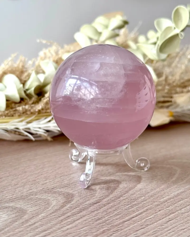 Sphère en quartz rose, pierre naturelle polie présentée sur un support transparent