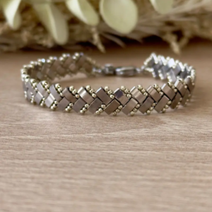 Bracelet Half Tila tissé motif chevrons argenté posé à plat sur fond bois