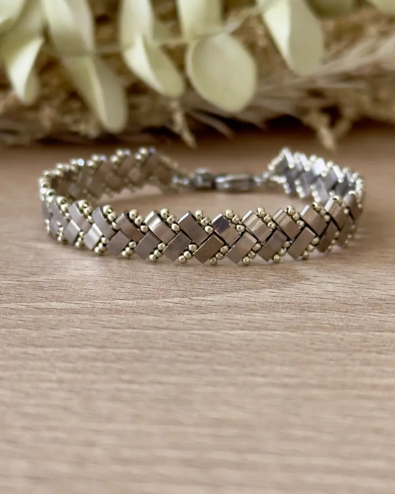 Bracelet Half Tila tissé motif chevrons argenté posé à plat sur fond bois