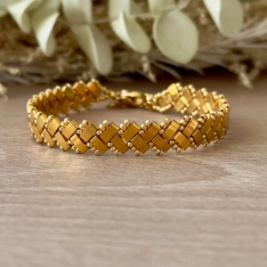 Bracelet Half Tila tissé chevrons doré gros plan sur fond bois