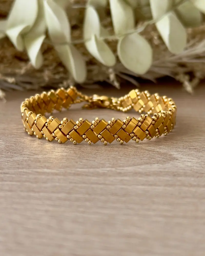 Bracelet Half Tila tissé chevrons doré gros plan sur fond bois