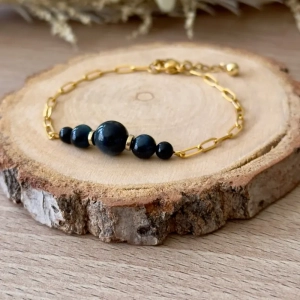 bracelet quintessence en acier inoxydable doré avec perles en œil de faucon posé sur rondin de bois