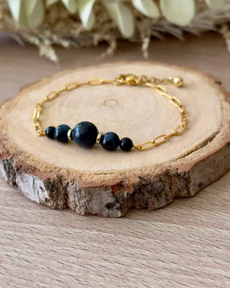 bracelet quintessence en acier inoxydable doré avec perles en œil de faucon posé sur rondin de bois