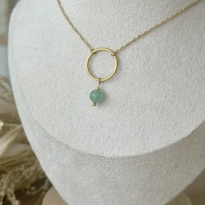 Collier NOLA en acier inoxydable doré avec pendentif cercle et perle en aventurine verte naturelle, présenté sur un buste beige dans une ambiance douce et naturelle.