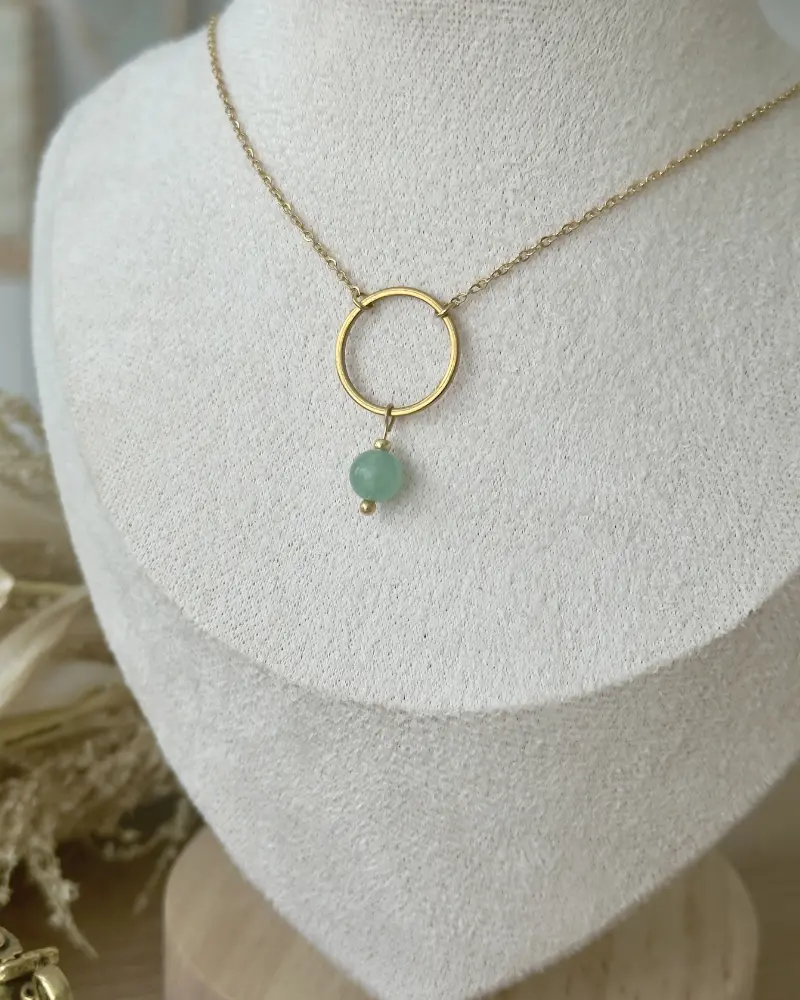 Collier NOLA en acier inoxydable doré avec pendentif cercle et perle en aventurine verte naturelle, présenté sur un buste beige dans une ambiance douce et naturelle.